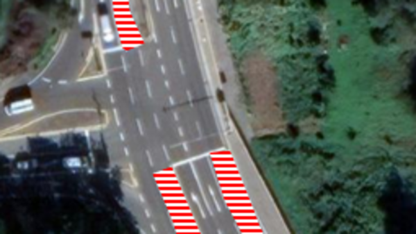 Eine Luftaufnahme einer Straße mit zwei Kurven, die mit roten und weißen Linien markiert sind. Die Umgebung besteht aus Grünflächen. Die Markierungen sollen wahrscheinlich die Fahrbahn oder spezielle Bereiche hervorheben.