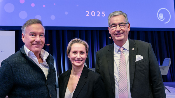 Drei Personen stehen lächelnd vor einem Hintergrund mit der Aufschrift „Herzlich Willkommen Neujahrsempfang 2025“. Die Gruppe posiert freundlich für ein Foto, der Fokus liegt auf der freundlichen Begrüßung des Neujahrsempfangs.