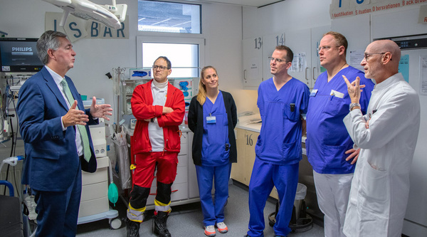 30.11.2023 - Besuch der zentralen Notaufnahme am Klinikum Ludwigsburg Eine Gruppe von sechs Fachleuten in einem Krankenhaus spricht miteinander. Ein Mann in Anzug erklärt etwas, während die anderen in medizinischer Kleidung zuhören. Es handelt sich um einen Austausch über Gesundheitsversorgung in einer modernen Umgebung.
