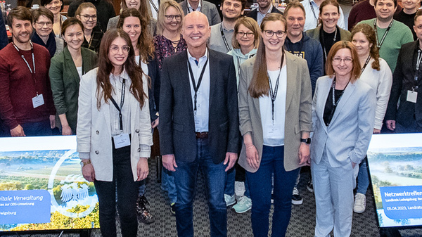 Un gruppo di circa 40 persone, tra cui studenti e relatori, si riunisce in un'aula conferenze. Alcuni partecipanti indossano abbigliamento formale, mentre altri sono casual. Due pannelli informativi con grafica sono posizionati di fronte al gruppo. L'atmosfera è di collaborazione e apprendimento.