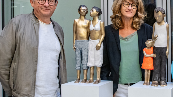 Vier Personen stehen neben Skulpturen von Kindern und Jugendlichen auf Podesten. Die Figuren sind aus Bronze und zeigen verschiedene Posen. Die Personen wirken miteinander im Gespräch, während sie die Kunstwerke betrachten.