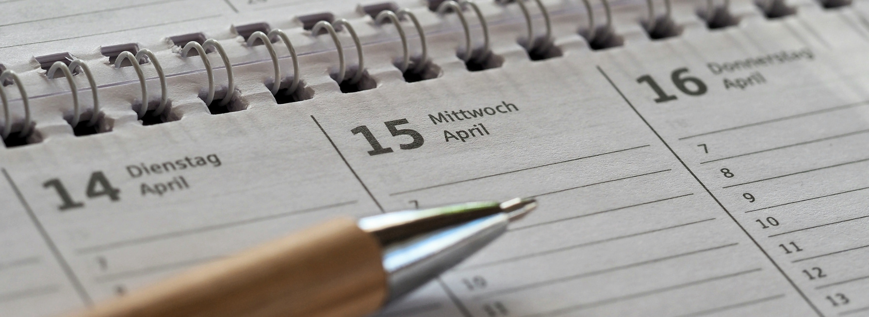 Header Bild: Ein aufgeschlagener Kalender zeigt den 15. April, Mittwoch, mit dem vorherigen Tag, dem 14. April, Dienstag, und dem folgenden Tag, dem 16. April, Donnerstag. Ein Stift liegt auf der Seite des Kalenders.