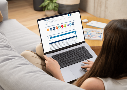 Eine Person sitzt entspannt auf einem Sofa und arbeitet an einem Laptop. Auf dem Bildschirm sind verschiedene Icons und eine Tabelle sichtbar, die Informationen und Daten anzeigen. Der Raum wirkt hell und modern eingerichtet.