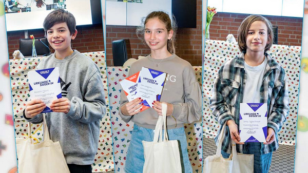 Drei Kinder stehen in einer Reihe und halten stolz ihre Urkunden in den Händen. Sie lächeln und tragen jeweils eine Umhängetasche. Im Hintergrund ist eine bunte Dekoration zu erkennen, die die festliche Atmosphäre unterstreicht.