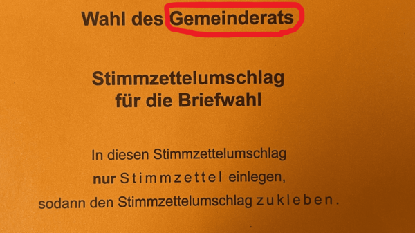 Das Bild zeigt ein orangefarbenes Dokument mit dem Titel "Wahl des Gemeinderats". Es betont, dass nur Stimmzettel für die Briefwahl in diesen Umschlag eingelegt werden dürfen. Der Hinweis auf die "Regionalversammlung" steht ebenfalls auf dem Dokument.