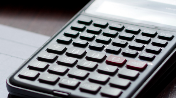 Ein schwarzer Taschenrechner liegt auf einer Oberfläche. Die Tasten sind deutlich sichtbar, darunter befindet sich eine numerische Tastatur. Der Bildschirm ist klar, aber momentan nicht in Benutzung.