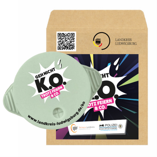 Eine Verpackung mit einem Aufkleber, der die Botschaft "Geh nicht KO trotz Feiern & Co." zeigt. Darunter befindet sich eine Internetadresse zur Aufklärung, kombiniert mit Logos von verschiedenen Institutionen, darunter die Polizei. Der Hintergrund ist bunt und auffällig gestaltet.