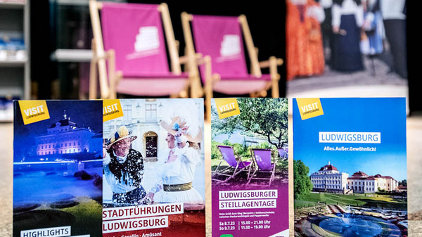 Immagine che mostra diversi depliant turistici su Ludwigsburg, in primo piano. I depliant offrono informazioni su attrazioni, tour guidati e opportunità di lavoro nella città. Sullo sfondo si vedono delle sedie e una esposizione di prodotti locali.