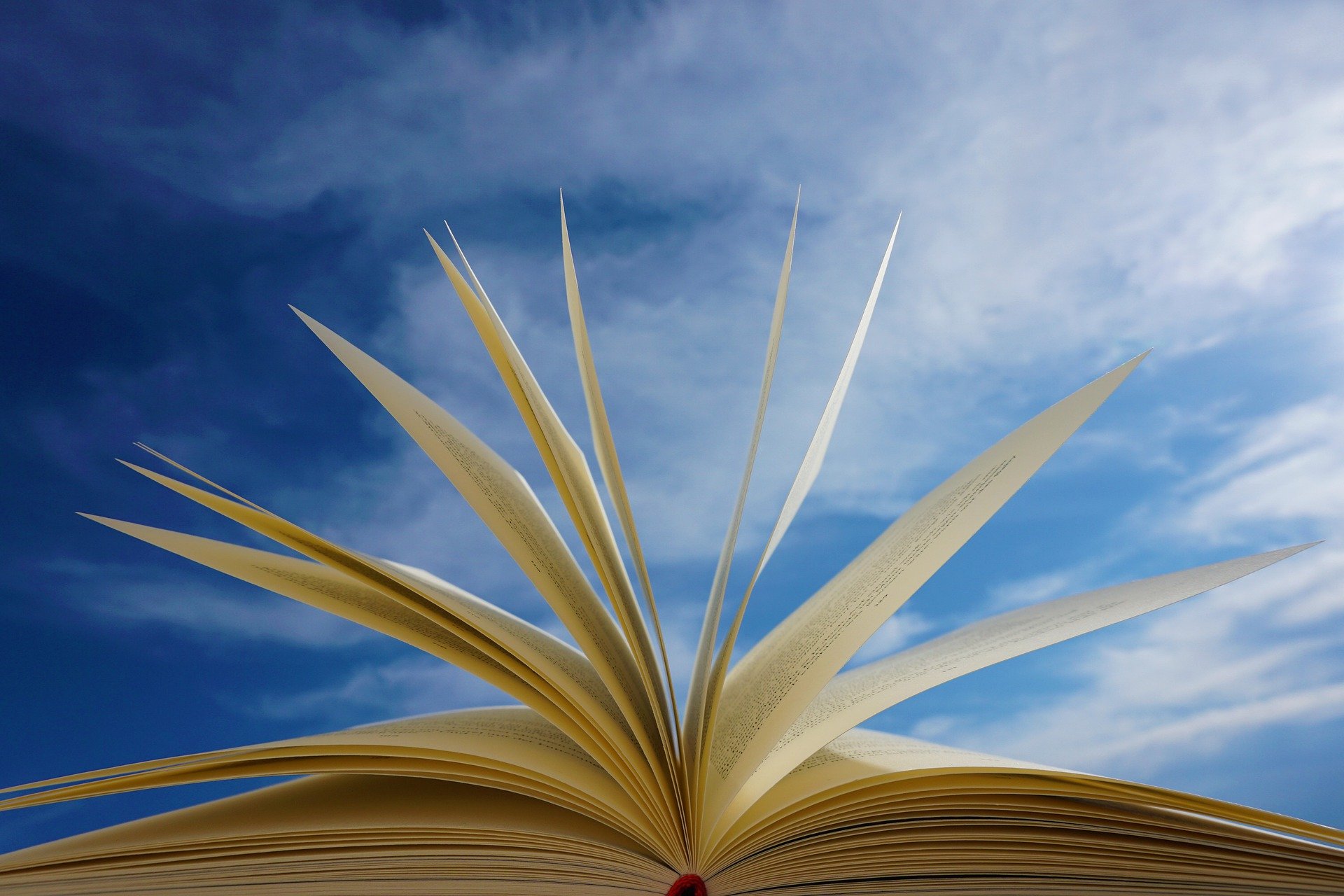 Ein aufgeschlagenes Buch wird von unten betrachtet, seine Seiten sind nach oben gewölbt und wirken lebendig. Im Hintergrund ist ein klarer, blauer Himmel zu sehen, der dem Bild eine inspirierende und luftige Atmosphäre verleiht.