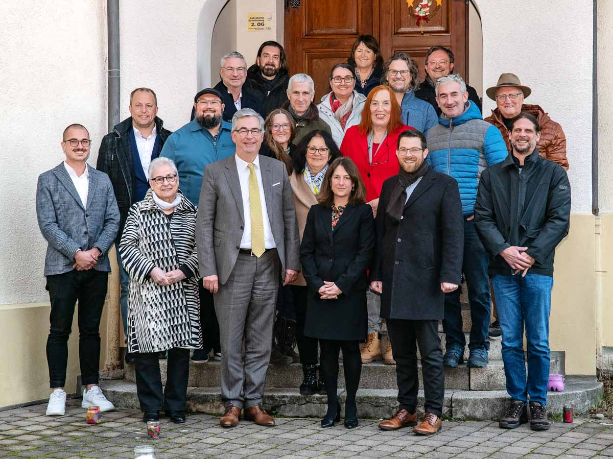 Un groupe de personnes se tient sur les marches d’un bâtiment. Elles semblent participer à un événement official. Les membres du groupe affichent des expressions variées, allant de sourires à des poses sérieuses, et sont habillés de manière formelle et décontractée.