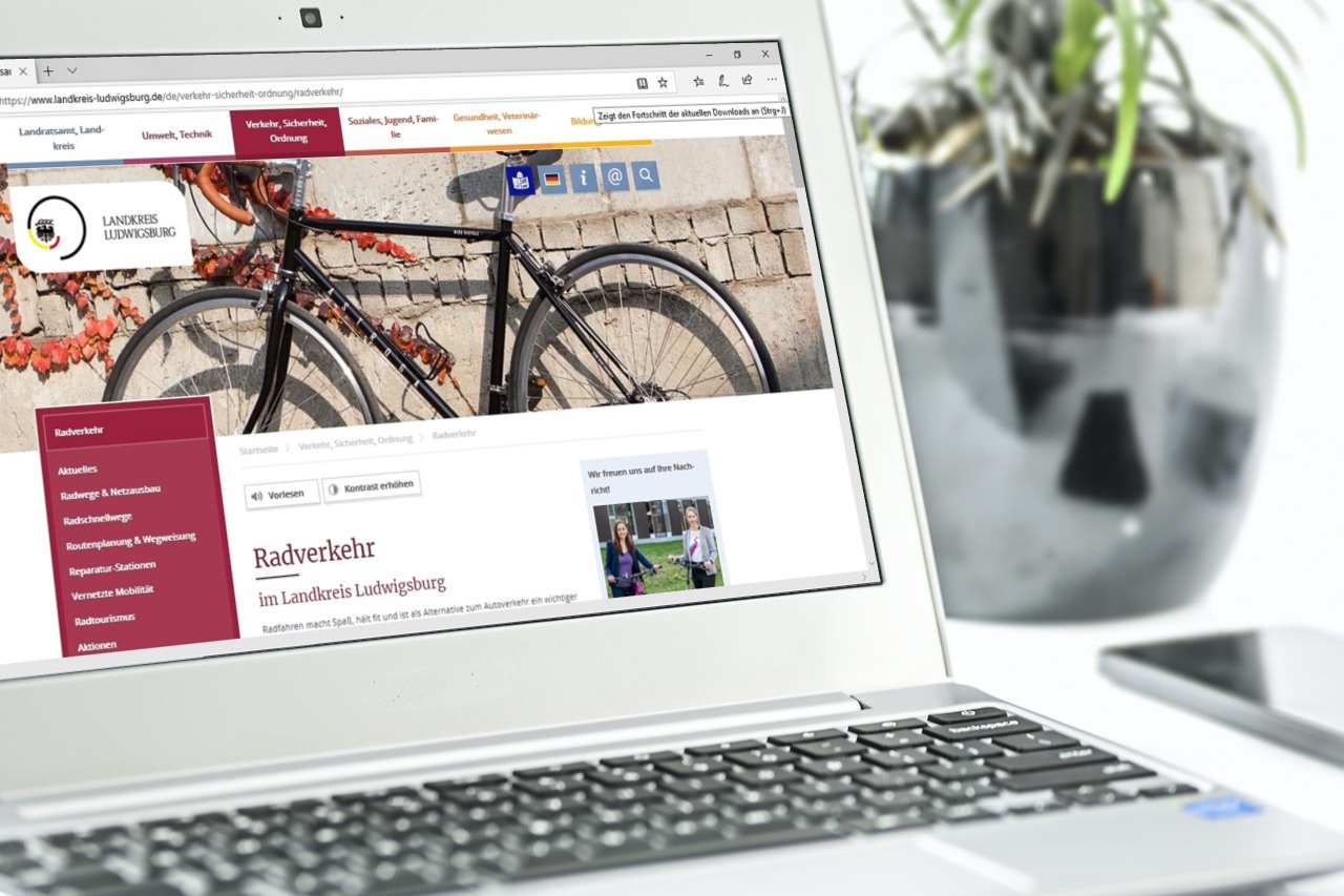 Ein Laptop zeigt eine Webseite des Landkreises Ludwigburg zum Thema Radverkehr. Im Hintergrund ist ein Fahrrad zu sehen, das an einer Mauer lehnt. Die Webseite beinhaltet Links zu verschiedenen Informationen und Dienstleistungen.