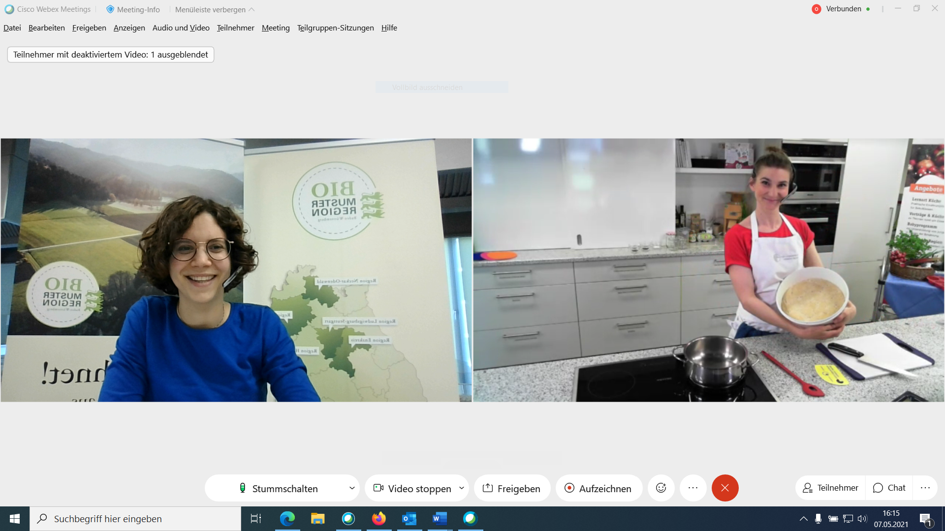 Ein Online-Workshop zur Zubereitung von Speisen. Eine Frau in einem blauen Oberteil lächelt von der linken Seite des Bildes, während eine andere Frau in einer weißen Schürze auf der rechten Seite eine Schüssel mit Teig hält. Hinter ihnen sind verschiedene Küchenutensilien und ein Banner sichtbar.