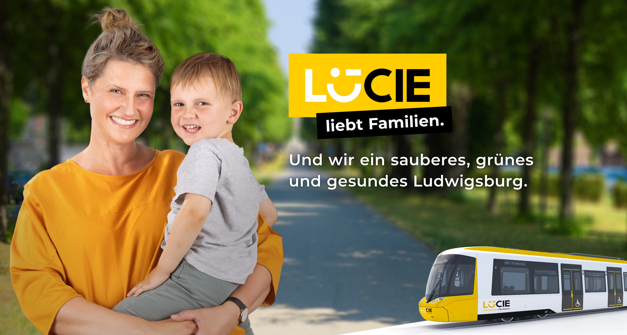 Eine Frau hält ein kleines Kind im Arm und lächelt. Im Hintergrund ist eine grüne Straße zu sehen. Der Text "LÜCIE liebt Familien. Und wir ein sauberes, grünes und gesundes Ludwigsburg." verdeutlicht das Engagement für eine familienfreundliche und umweltbewusste Stadt.