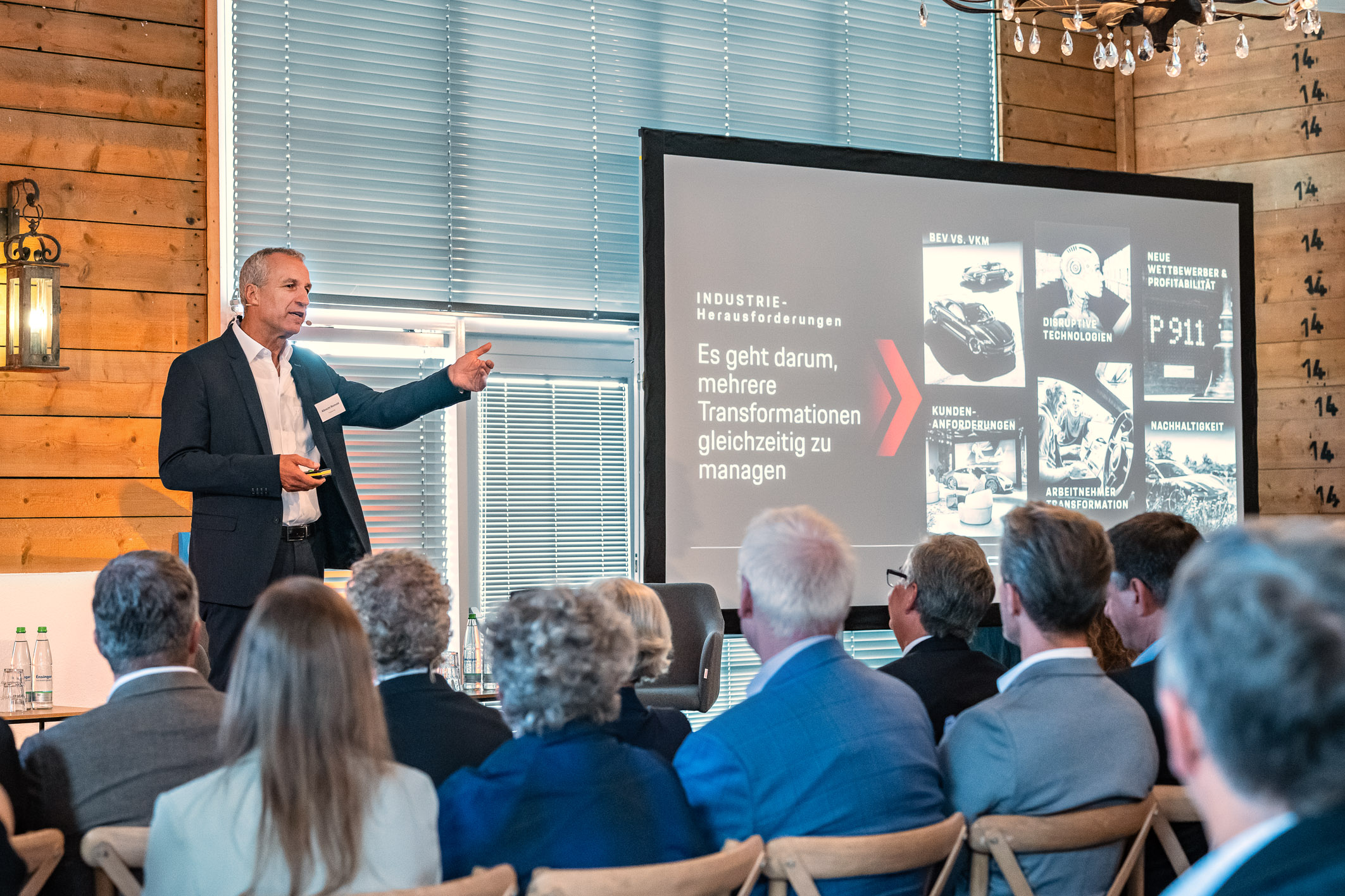 Eine Präsentation auf einer Konferenz, bei der ein Referent mit einem Diagramm spricht, das verschiedene Industriebereiche und Herausforderungen zeigt. Der Fokus liegt auf der Aussage zur gleichzeitigen Bewältigung mehrerer Transformationen. Im Hintergrund sitzen Zuhörer, die dem Vortrag folgen.