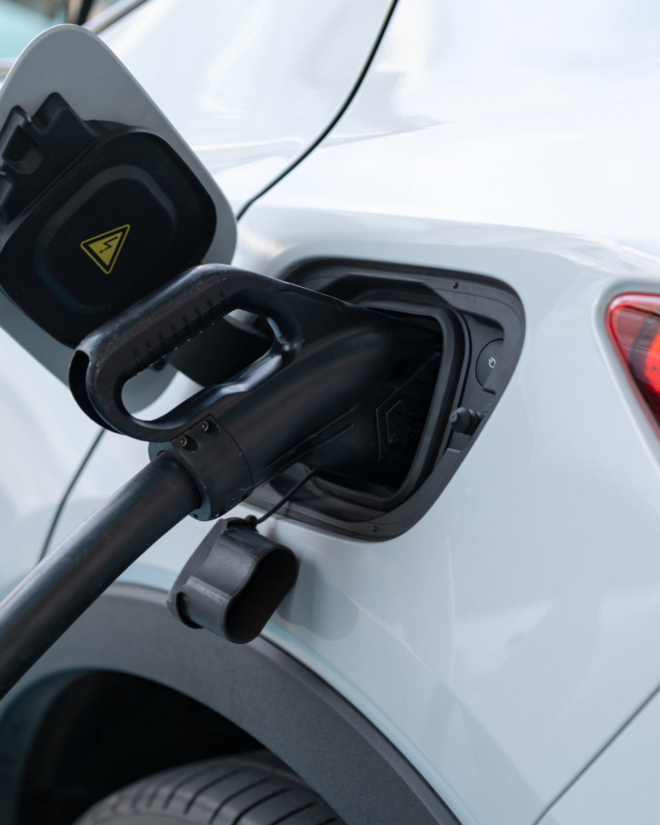 Ein weißes Auto tankt an einer Tankstelle. Der Kraftstoffschlauch ist in die Tanköffnung gesteckt, während der Tankdeckel geöffnet ist. Das Bild zeigt den Tankvorgang eines Fahrzeugs.