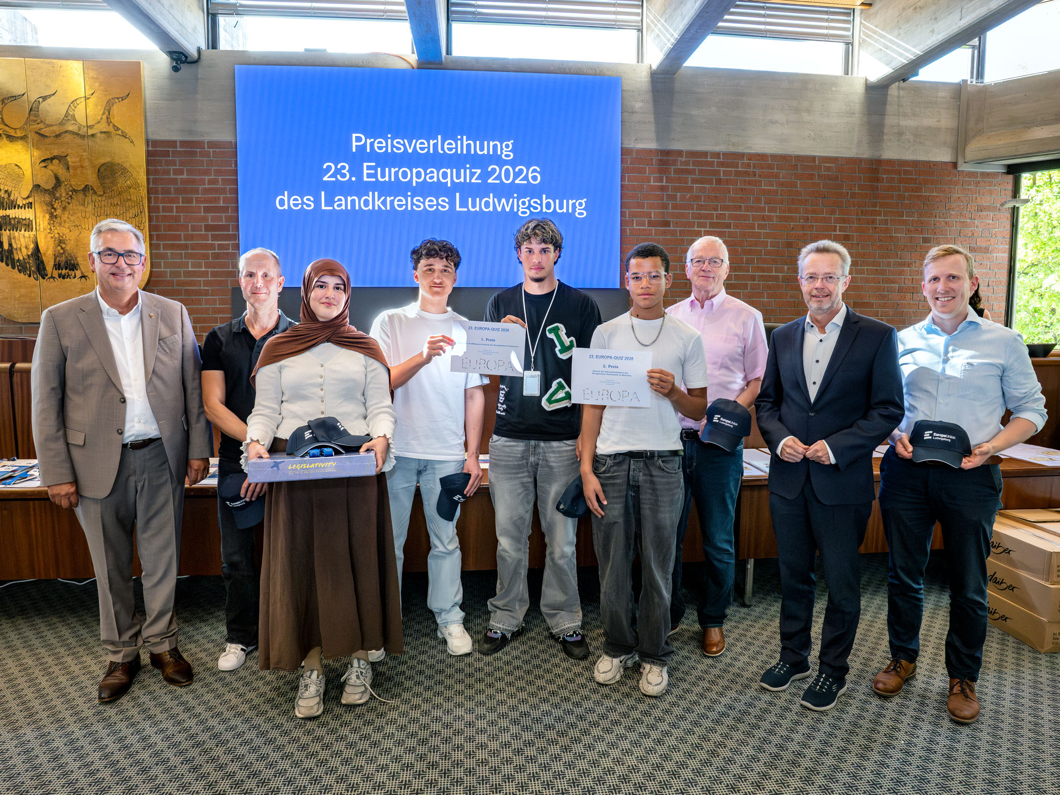 Gruppenfoto von Teilnehmern der Preisverleihung des 23. Europaquiz 2026 des Landkreises Ludwigsburg. Die Gewinner halten Urkunden und tragen schwarze Kappen. Im Hintergrund steht ein Bildschirm mit dem Titel der Veranstaltung. Es sind insgesamt sieben Personen zu sehen, darunter auch zwei Frauen.