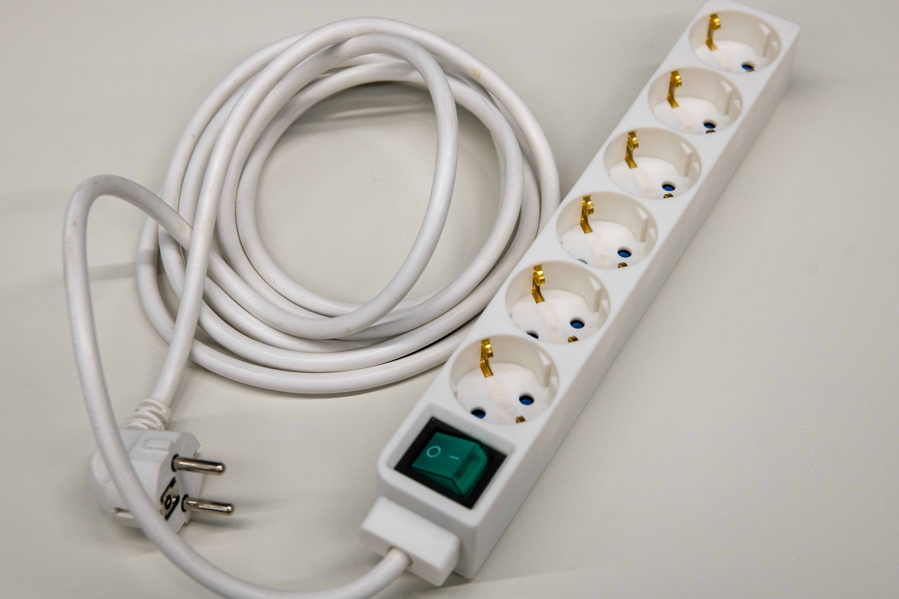 Eine weiße Steckdosenleiste mit sechs Steckdosen und einem abschaltbaren Schalter. Ein längeres Kabel hängt an einer Seite, während die andere Seite mit einem Standardstecker ausgestattet ist.