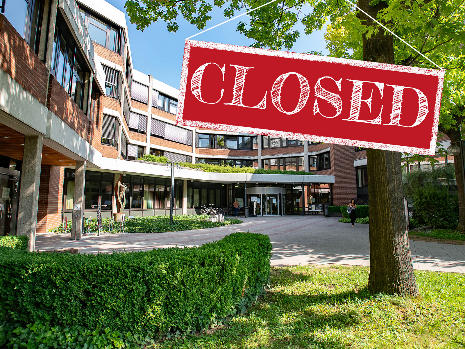 Das Bild zeigt einen Eingangsbereich eines Gebäudes mit einem deutlich sichtbaren Schild, auf dem "CLOSED" in großen roten Buchstaben steht. Die Umgebung ist hell und freundlich, mit Bäumen und gepflegten Grünflächen, aber das Gebäude ist geschlossen. (Text KI generiert)