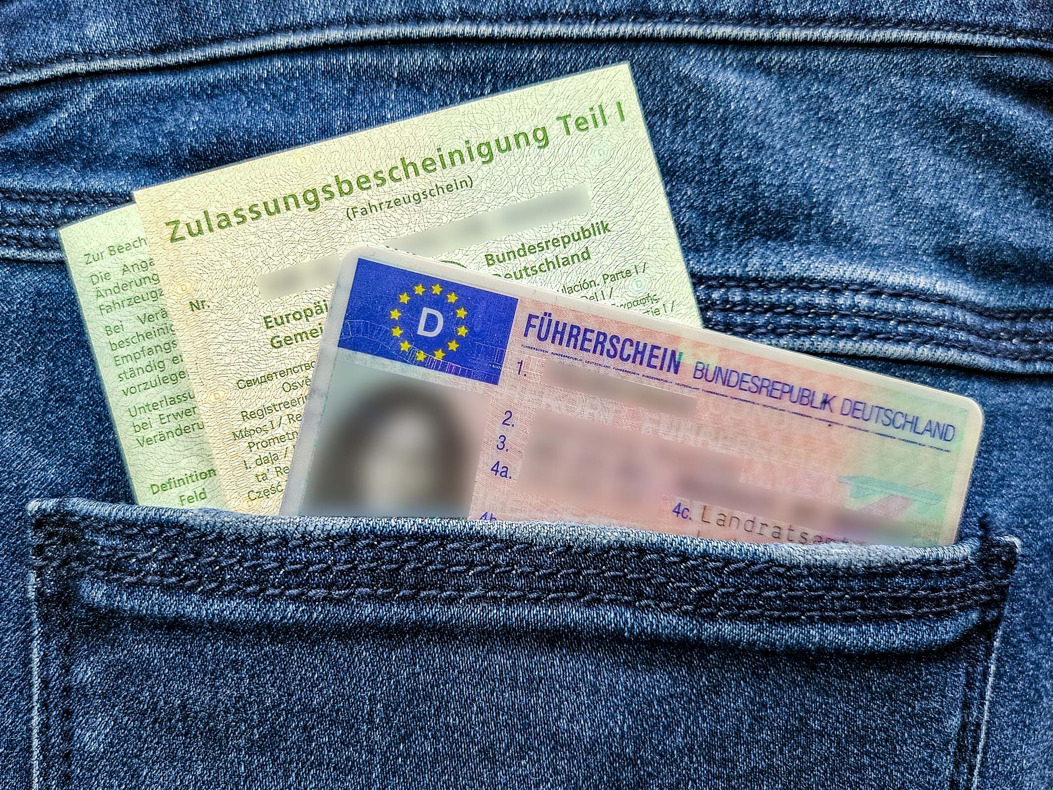 Two driver's documents are partially visible in a pocket of blue denim jeans. The top document is a green vehicle registration certificate, while the bottom document is a German driver's license, displaying multiple fields and official markings.