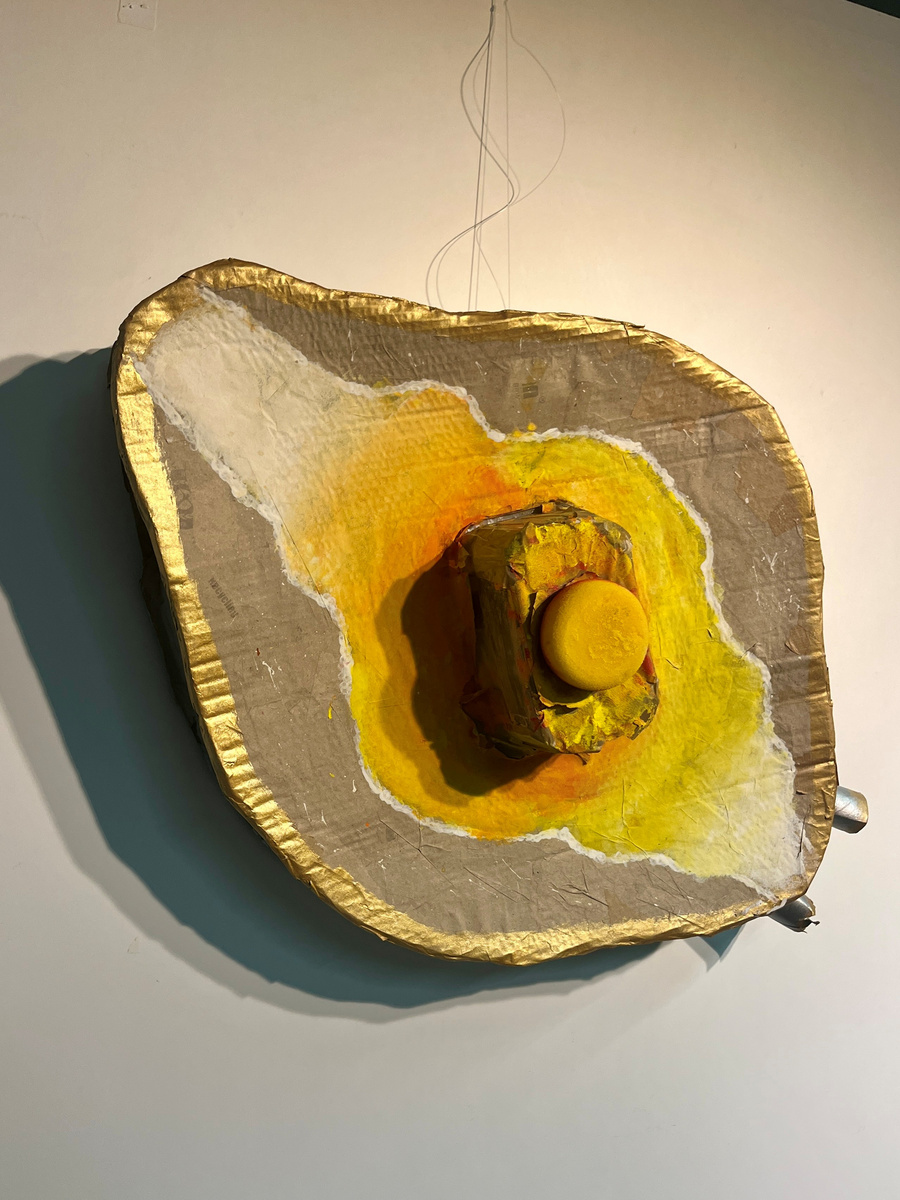Eine dreidimensionale Kunstinstallation, die ein Spiegelei darstellt. Die glänzende, goldene Umrandung umrahmt eine gelbe, runde Form in der Mitte. Die Farben variieren von hellgelb zu orange und beige, wobei eine strukturierte Oberfläche und eine interessante Formgebung auffallen.