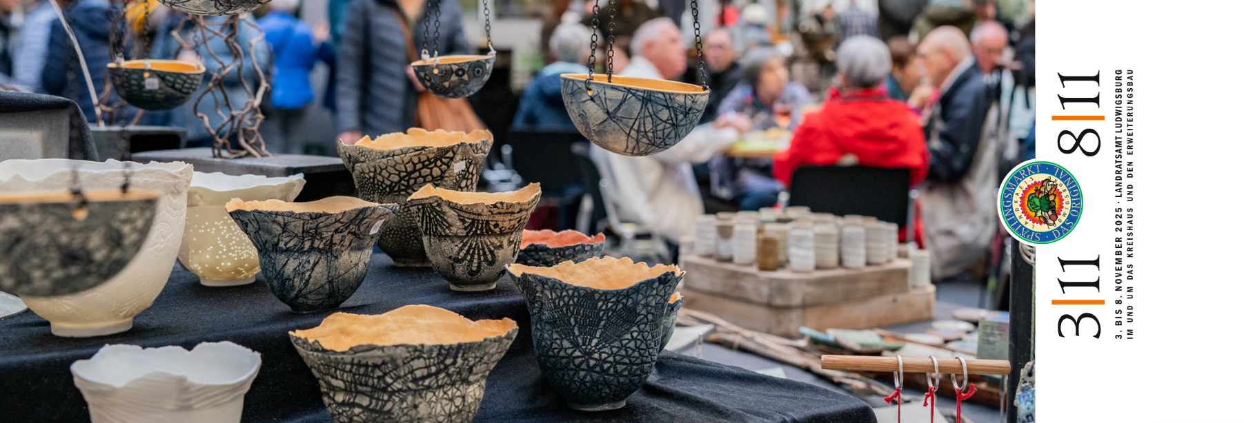 Auf dem Bild sind kunstvolle Schalen in verschiedenen Farben und Mustern zu sehen, die auf einem Markt ausgestellt sind. Im Hintergrund sind Menschen zu erkennen, die sich unterhalten und das Ambiente genießen.